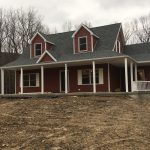 A red house with a porch is sitting on top of a dirt hill.