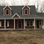 A red house with a gray roof and a porch in the middle of a field.