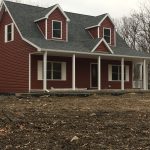 A red house with a porch is sitting in the middle of a dirt field.