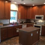 A kitchen with wooden cabinets , a sink , stove , microwave and a window.