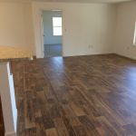 An empty living room with hardwood floors and a door leading to a kitchen.